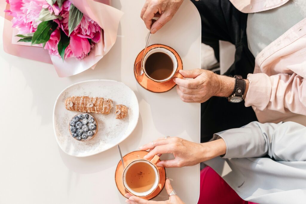 pexels-photo-8790886-8790886 Top view of two people enjoying coffee and pastries at a table adorned with flowers.