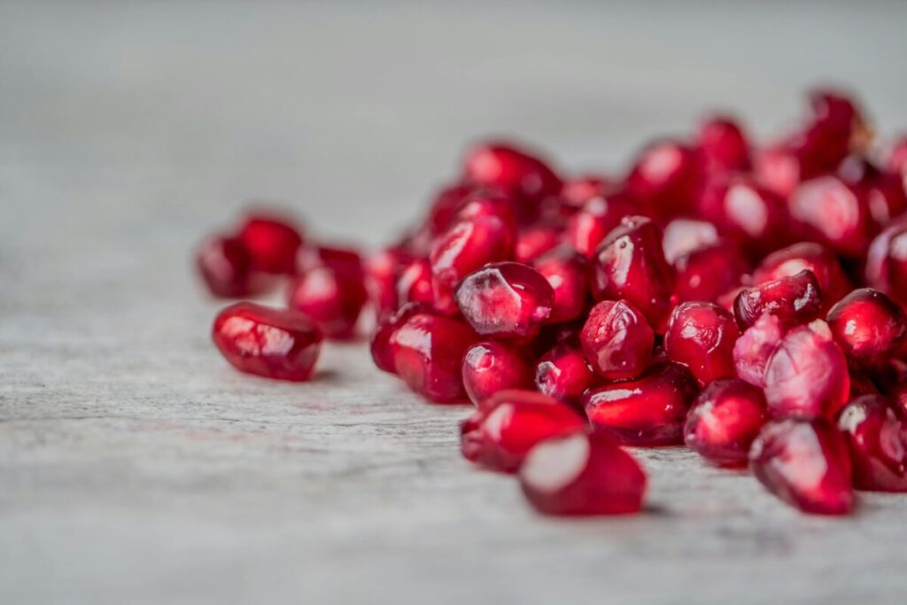 Vivid close-up of juicy red pomegranate seeds scattered on a surface.
